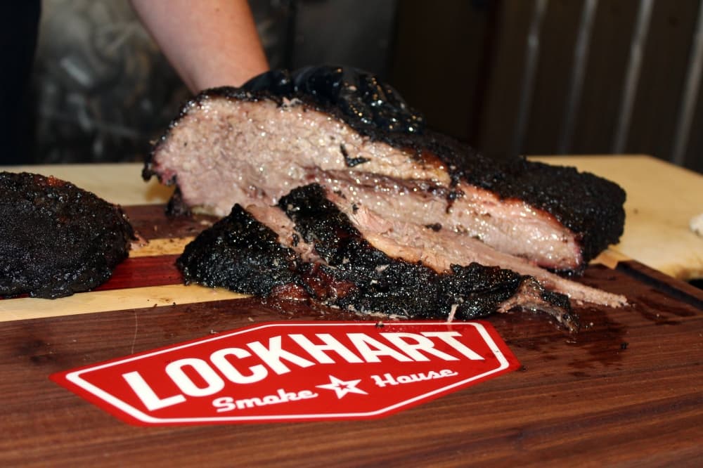 Person cutting brisket on a wooden cutting board with Lockhart logo.