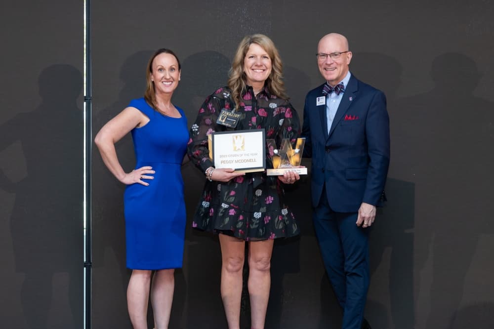 three people pose together with an award