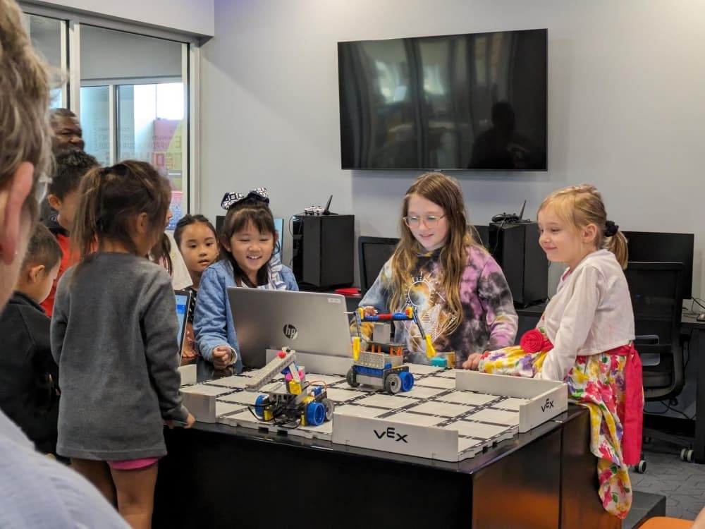 children crowd around table with computer controlled robots