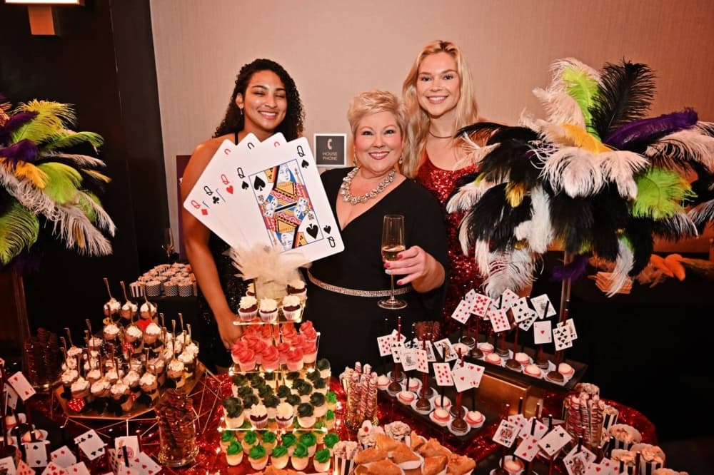 Three females standing by a desert table. 