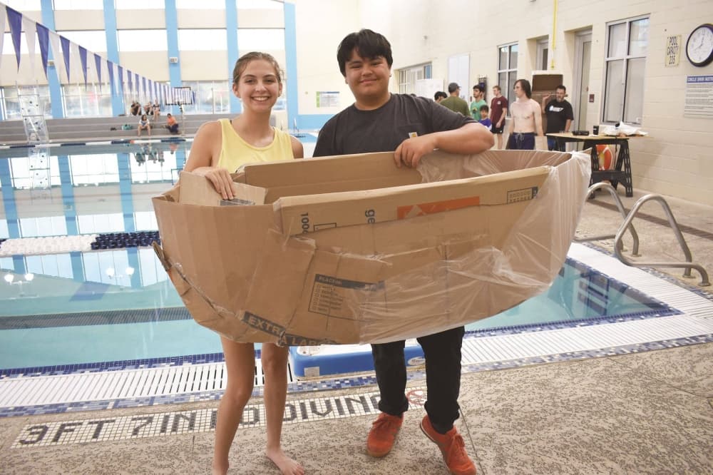 A girl and boy holding a handmade boat.