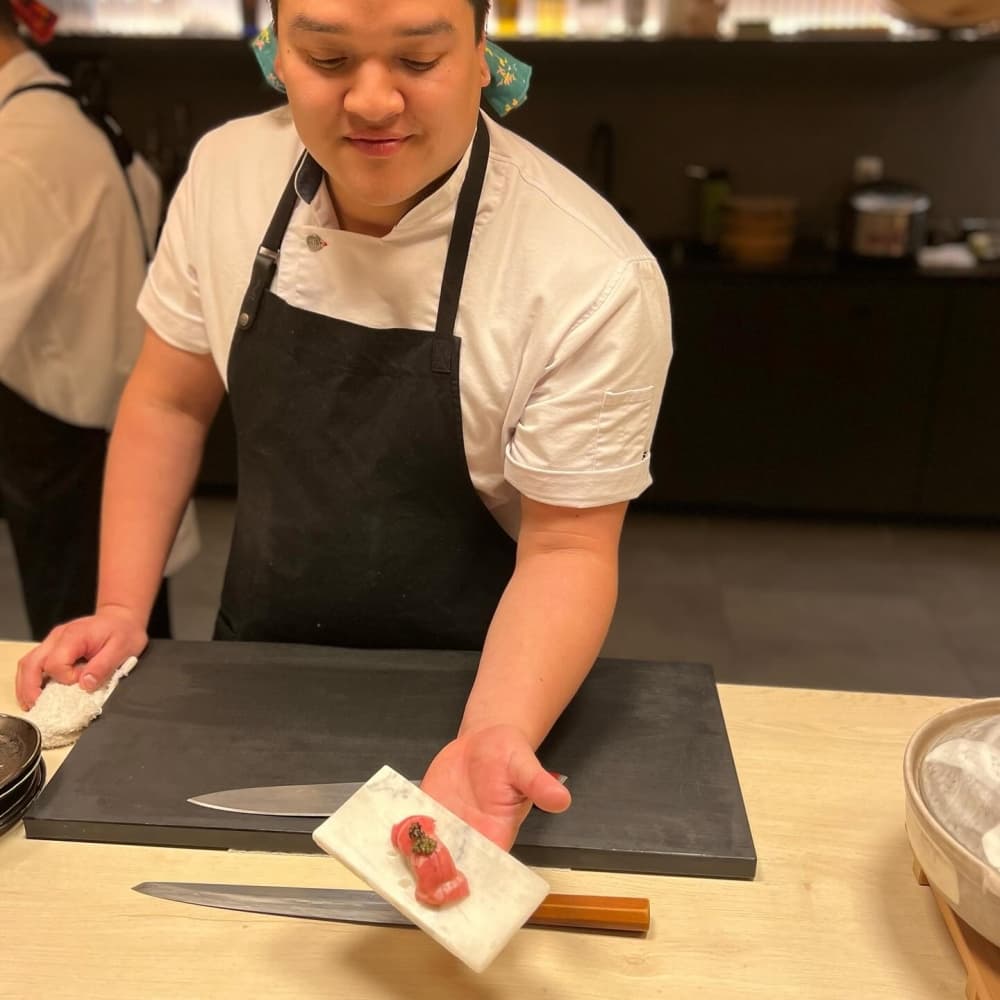 The chef presents a piece of fish from behind the counter.