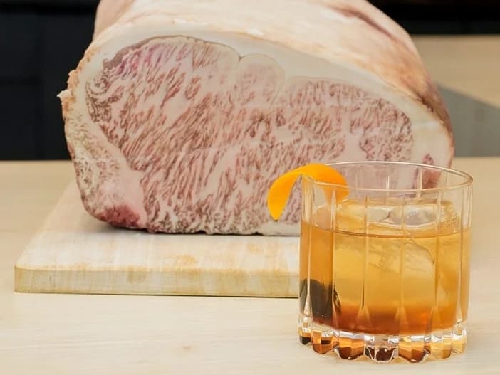 A brown drink is shown in front of a slab of Wagyu beef.
