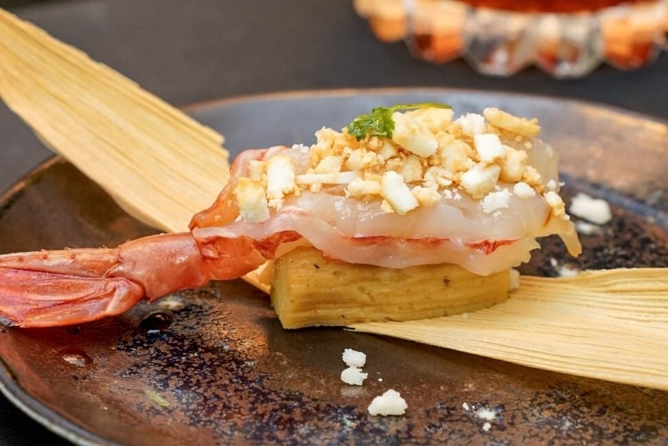 A shrimp sits on a tamale on a black plate.