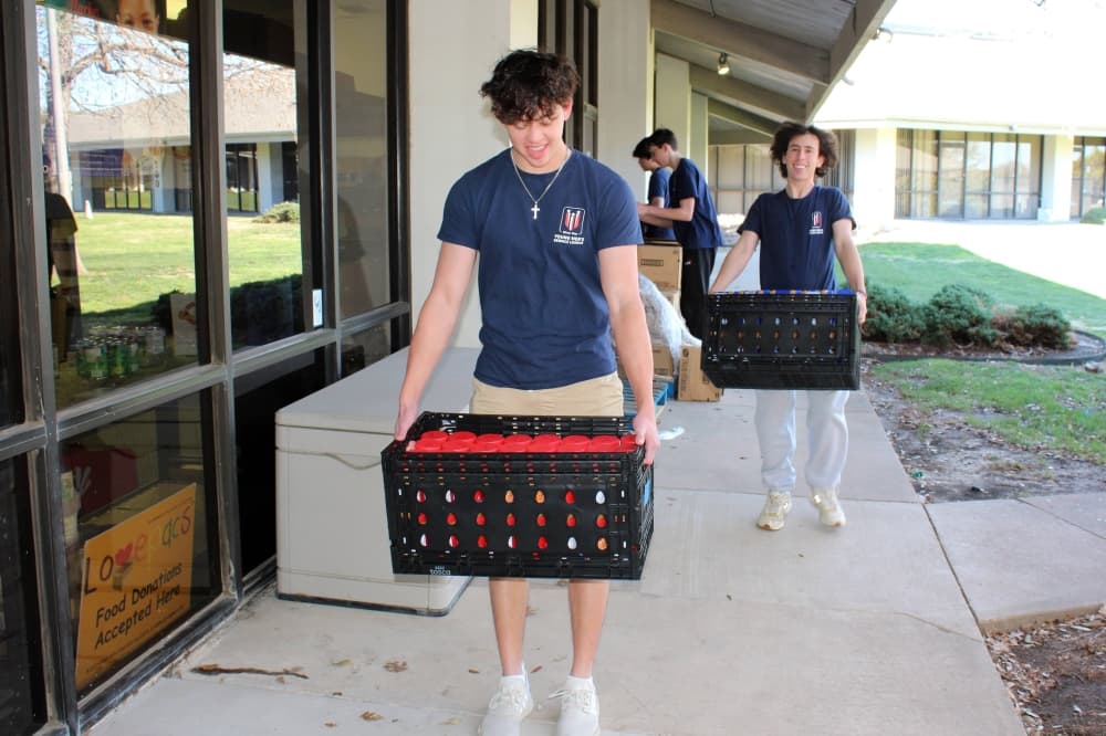 Two males carrying plastic crates next to an office building.