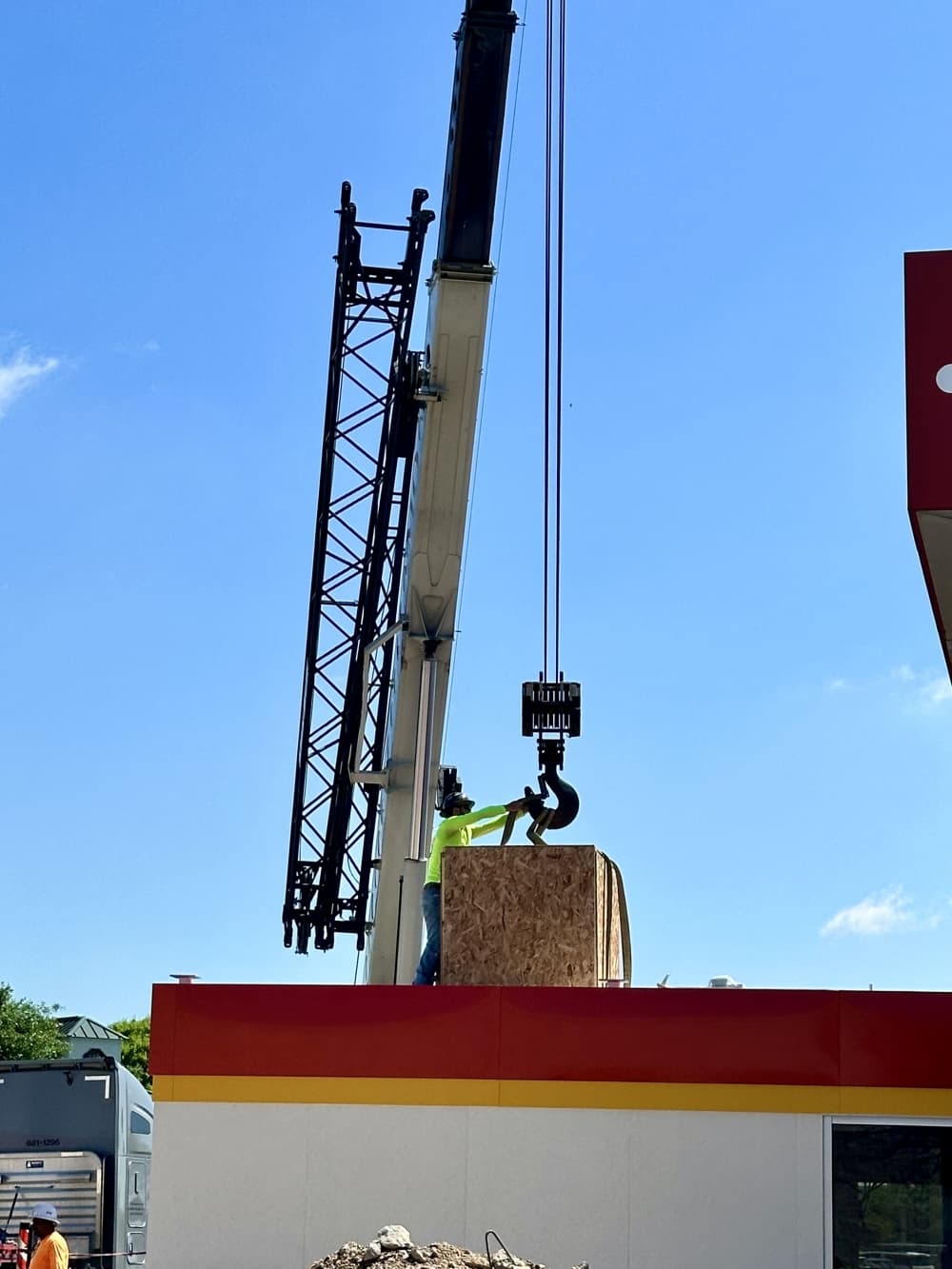 A worker guides a crane holding a wooden box on top of the fuel kiosk.