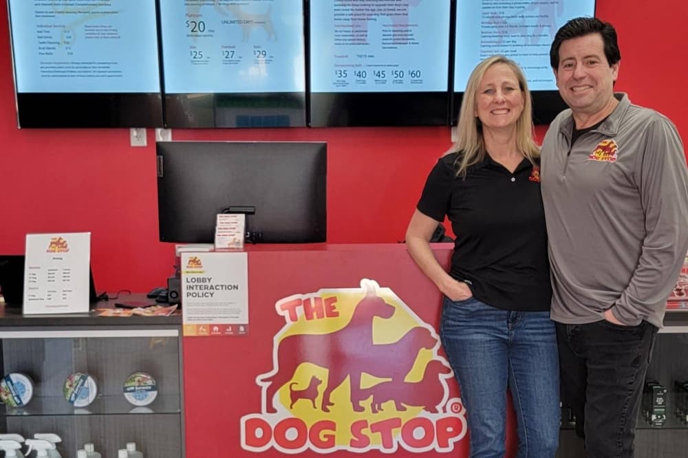 Male and female standing in front of a business counter with The Dog Stop sign.