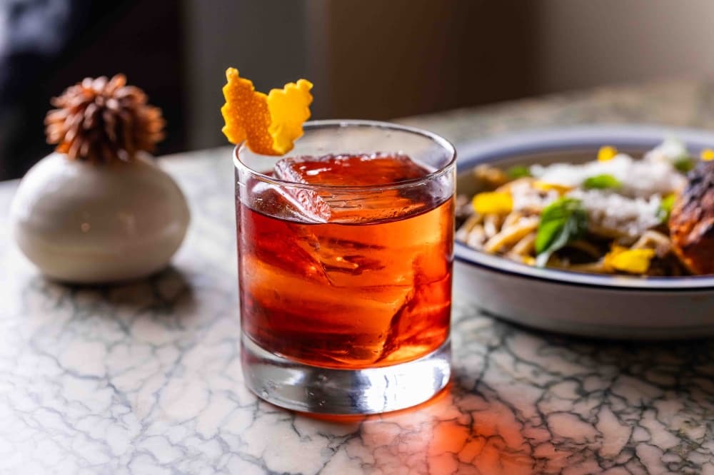 A brown drink is shown on a table with food behind it.