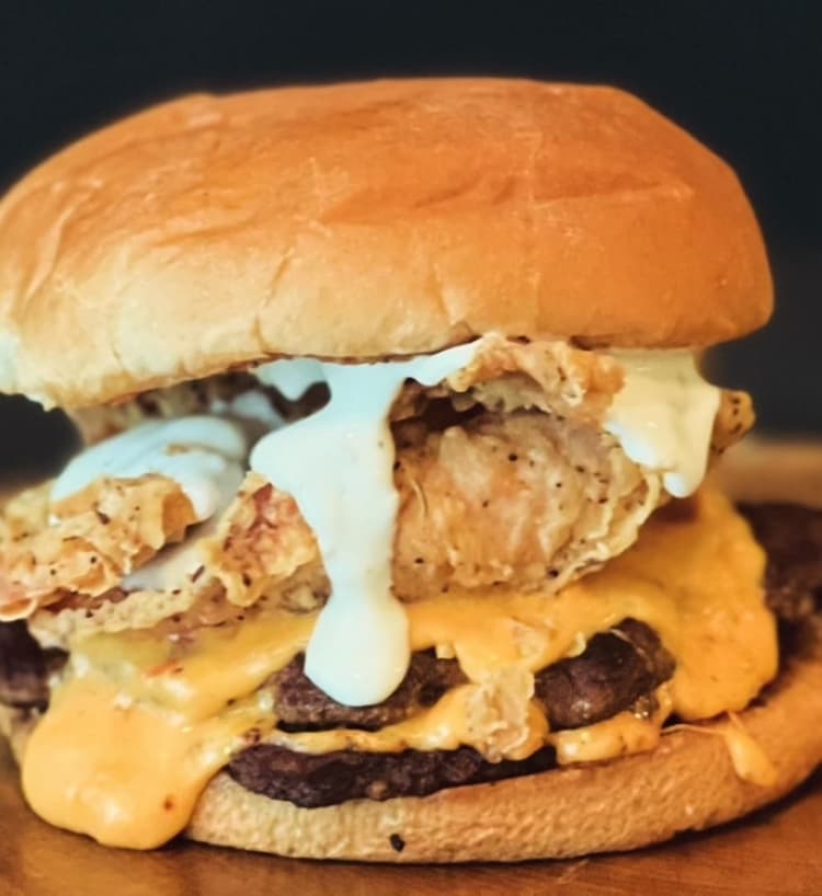 A chicken sandwich is covered in cheese and sauce.