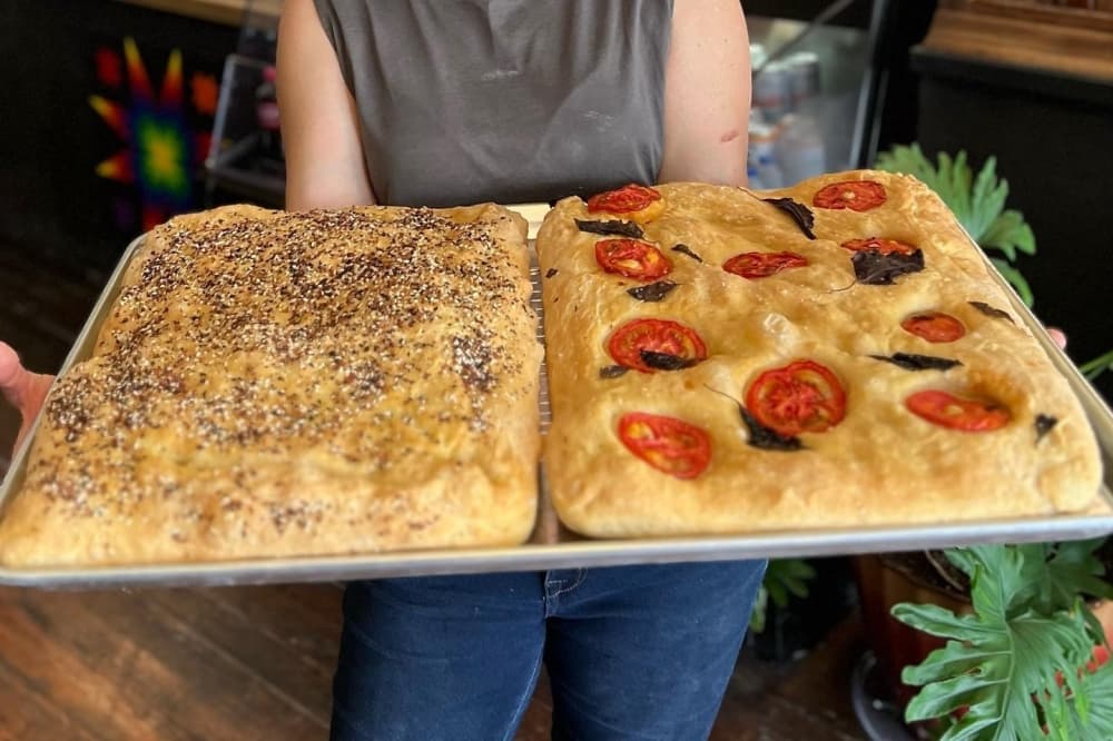 A person holds a tray with two big focaccia loaves.