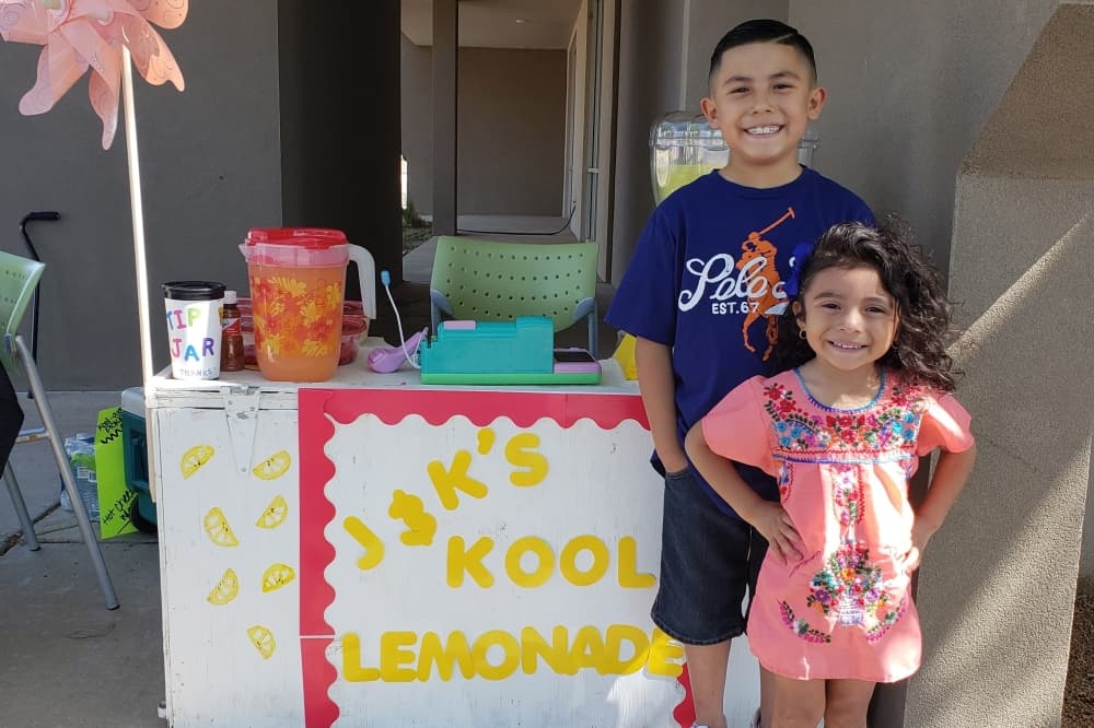 Two children pose next to their lemonade stand.