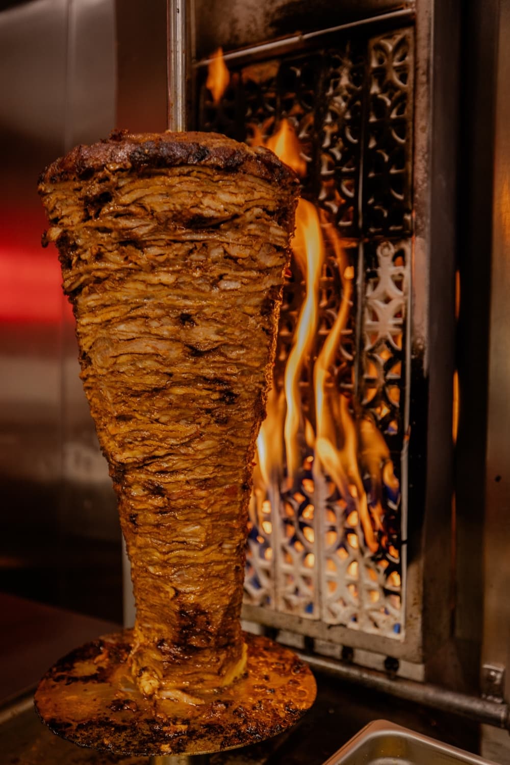 Meat on a spinning rotisserie is shown with fire in the background.