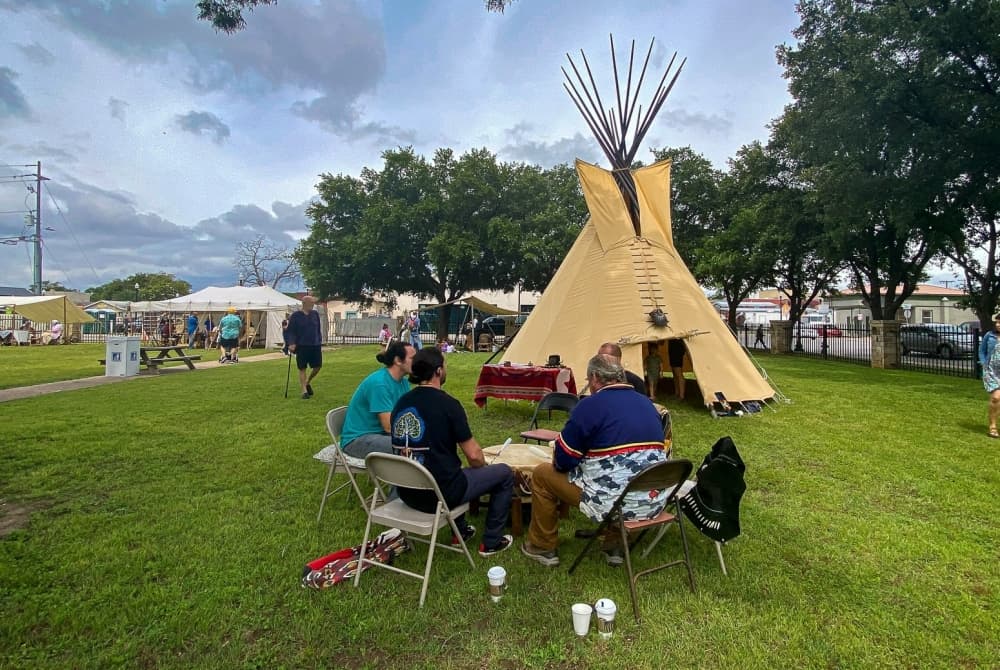 A teepee is shown with people sitting around it.