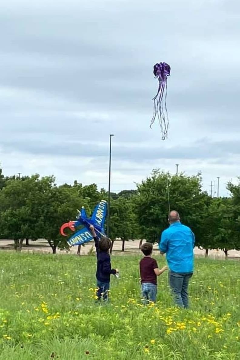 Three people flying a kite in a flower filled field.