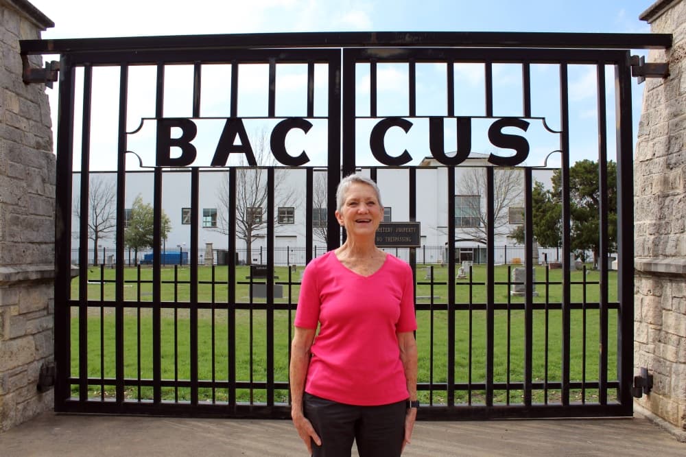 Woman standing in front of iron gate with the word BACCUS on the gate doors.