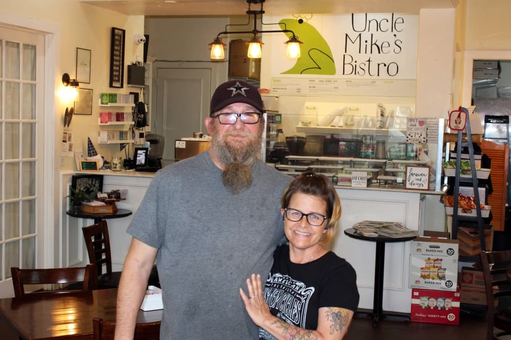 Man and woman standing in a restaurant with Uncle Mike's Bistro signage. 