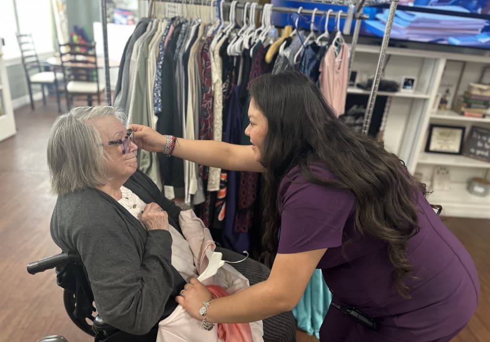 The caregiver holds up a pair of earrings next to a woman's ears.