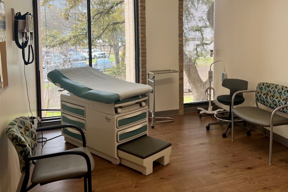 The interior of an exam room is shown with windows in the background.