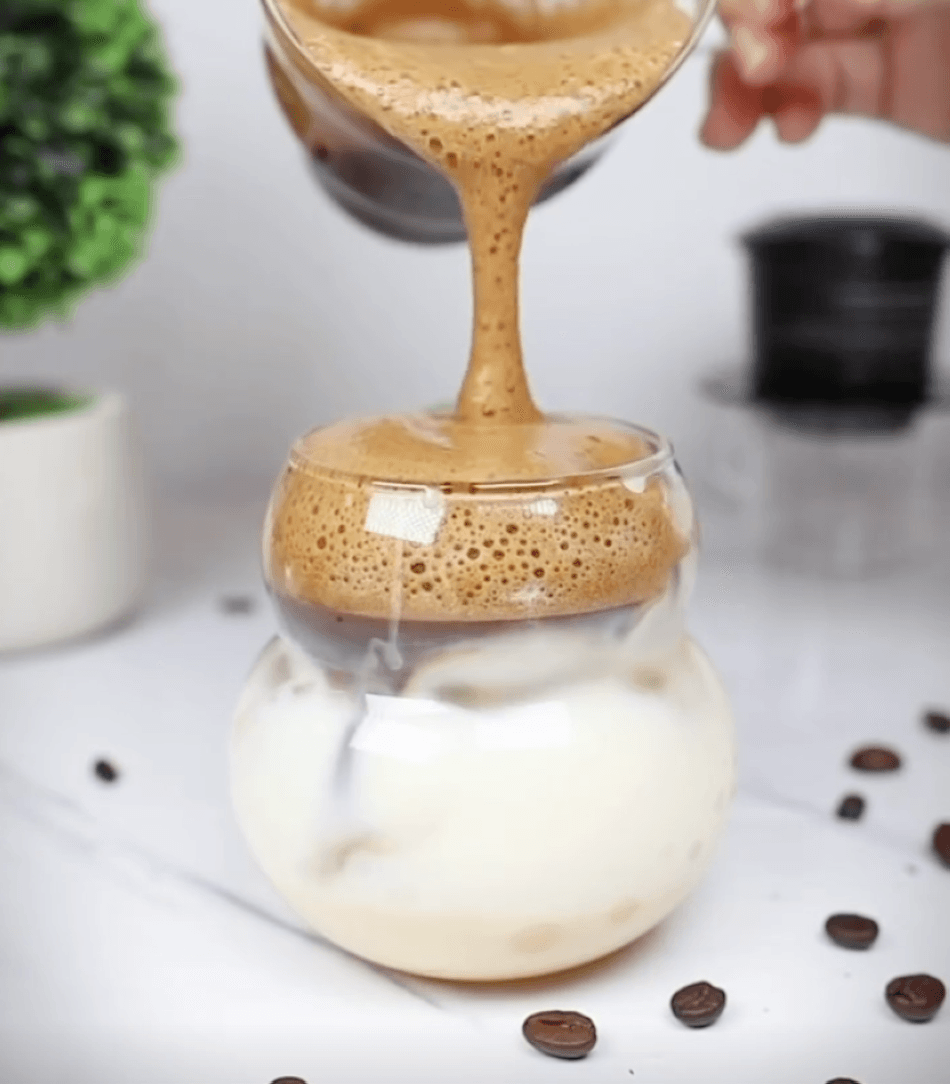 A glass of brewed coffee is poured into another glass with sweetened condensed milk.