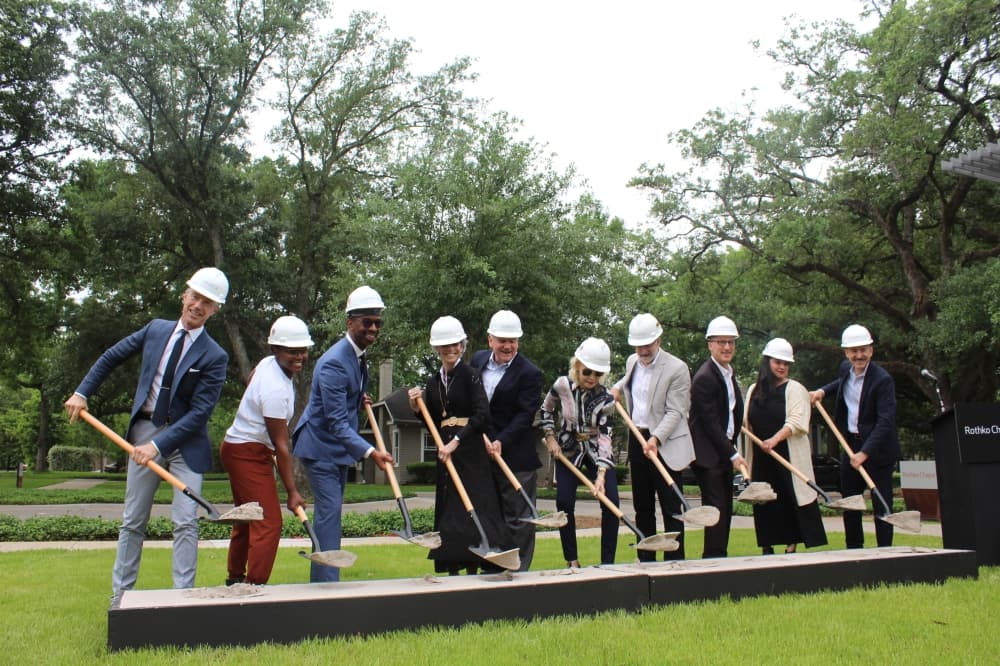 a row of people hold shovels of dirt at a ceremonial ground breaking