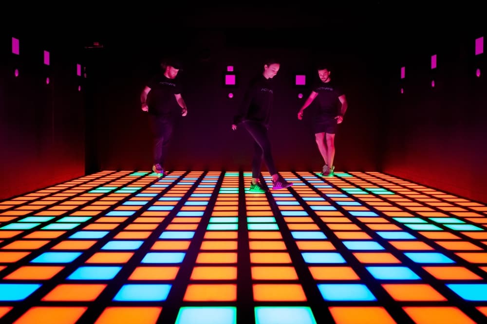 A small group of people in a room with various colored square lights on the ground.