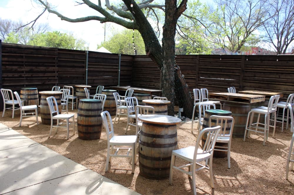 Multiple chairs situated next to multiple wooden barrel tables outside.