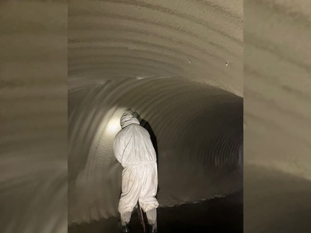 A worker applies an epoxy to the interior of an underground culvert