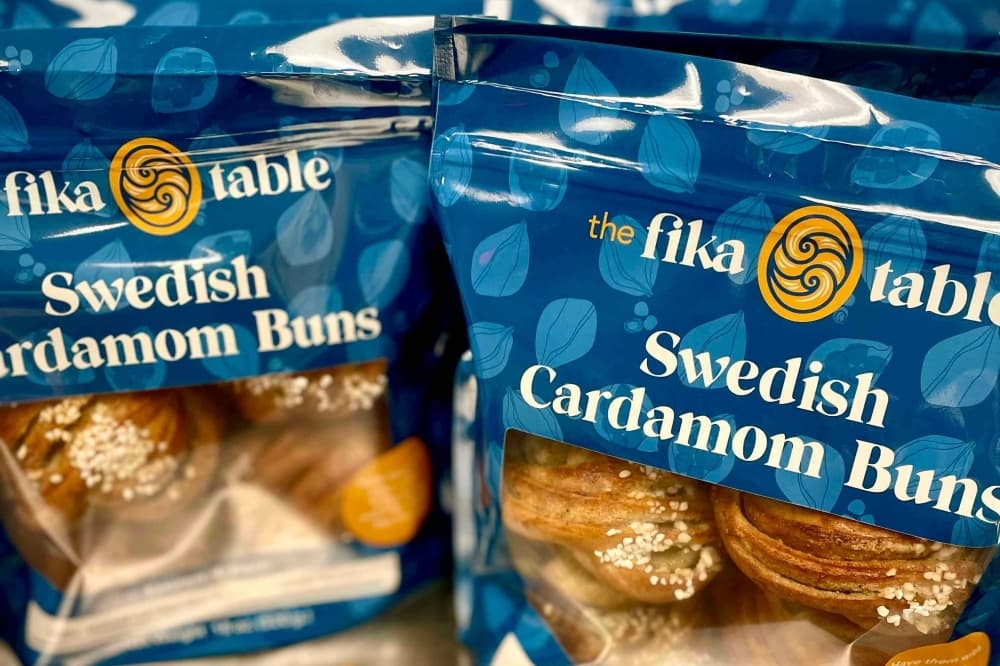 Blue bags with The Fika Table's logo in white letters are shown with four buns inside.