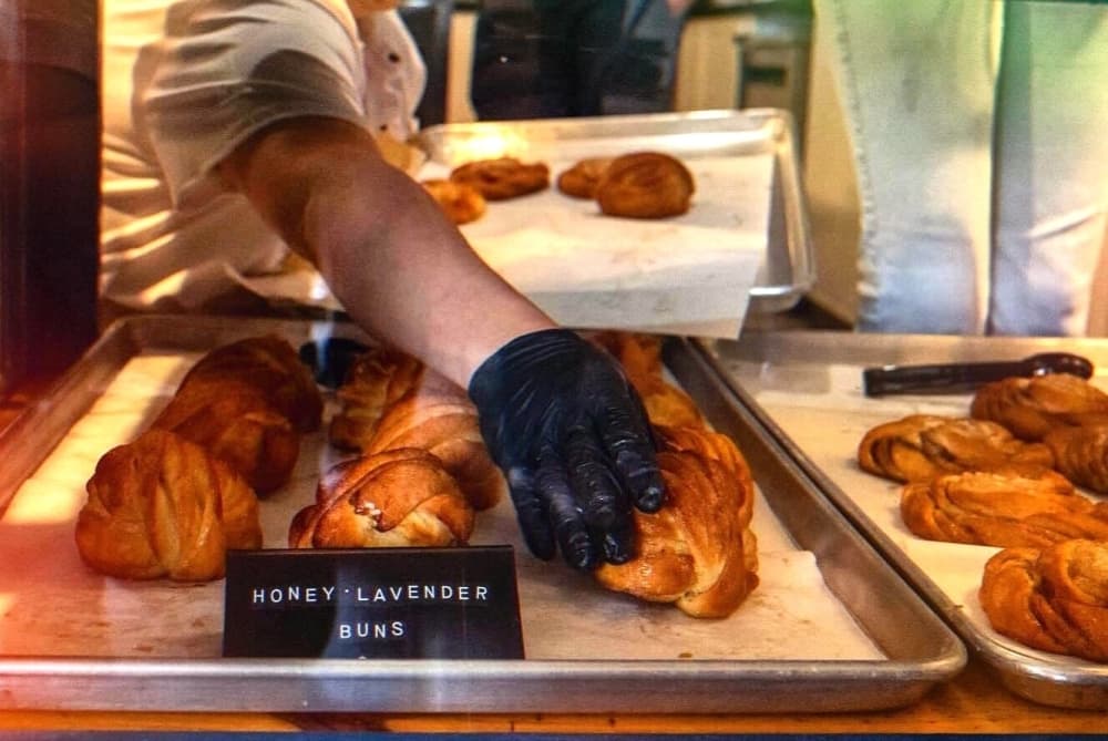 A baker arranges honey lavender buns in a display case.