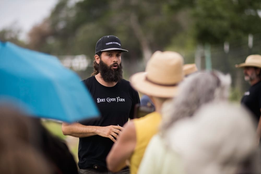 A man speaks to a group of people at a farm.