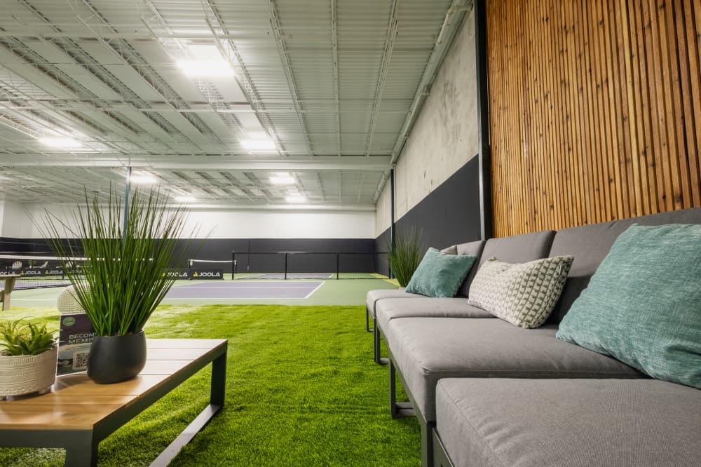 A lounge area is shown at the pickle ranch with grey couches will pillows next to a table with plants.