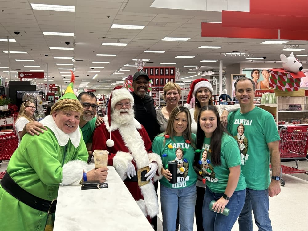 People in green pose with Santa and a Christmas elf.