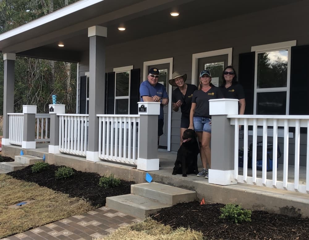 Four people stand on the steps of a newly constructed house.