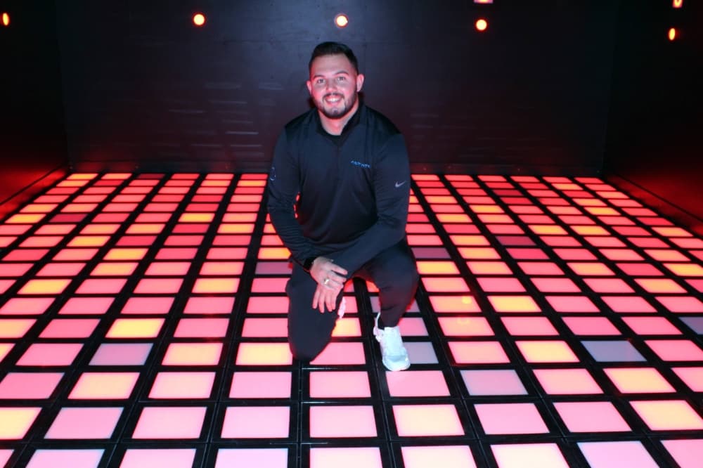Man kneeling on floor made of different colored lights.