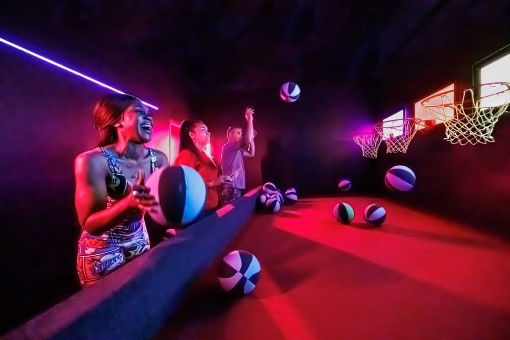 People in a darkened room playing carnival style baketball games. 