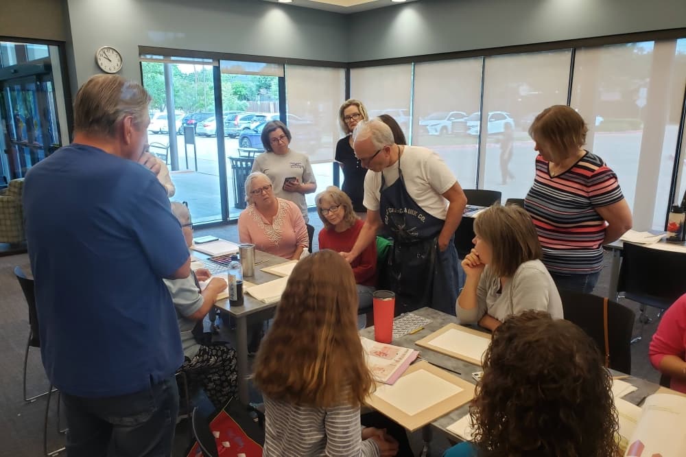 Group of people gathered around a table painting on paper. 
