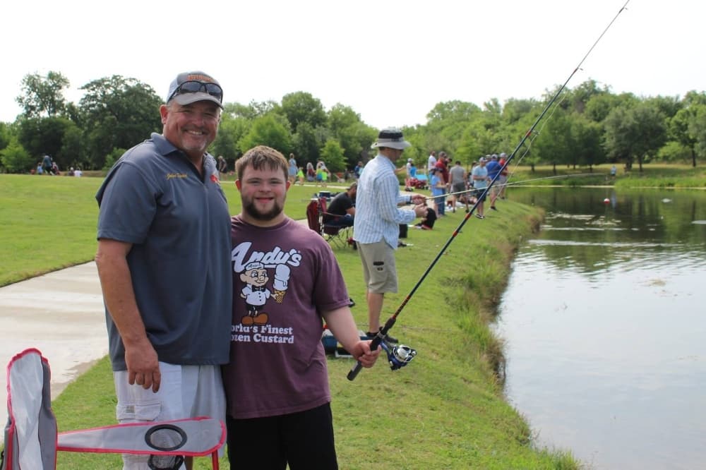 Two males near a pond with a fishing rod.