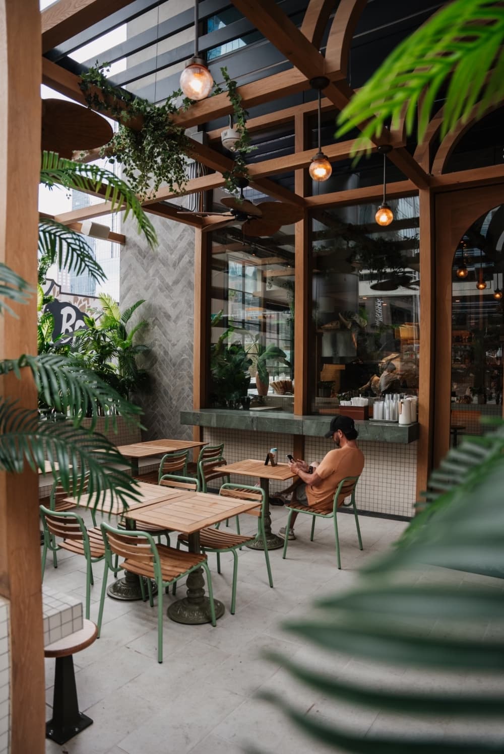 The patio is shown with tall windows between the indoor and outdoor areas, and green plants scattered throughout the space.