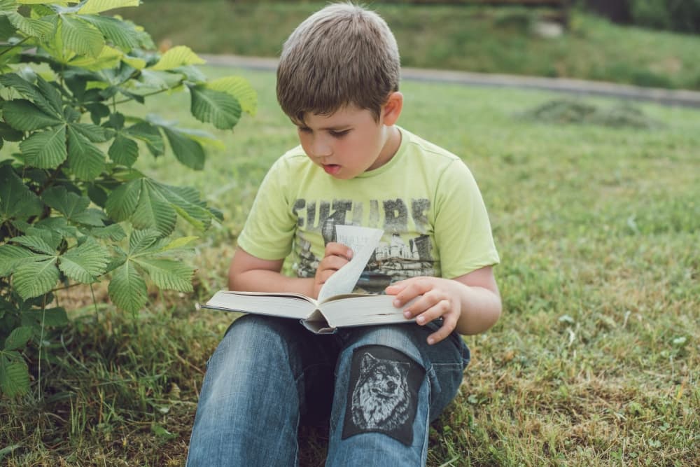 A boy sits outside reading a book.