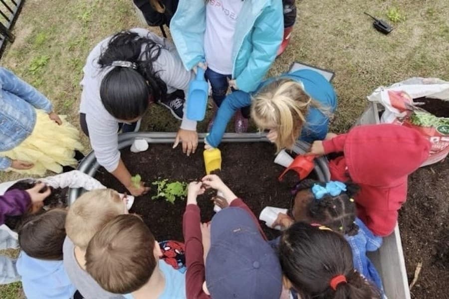 a group of children work in a flowerbed 
