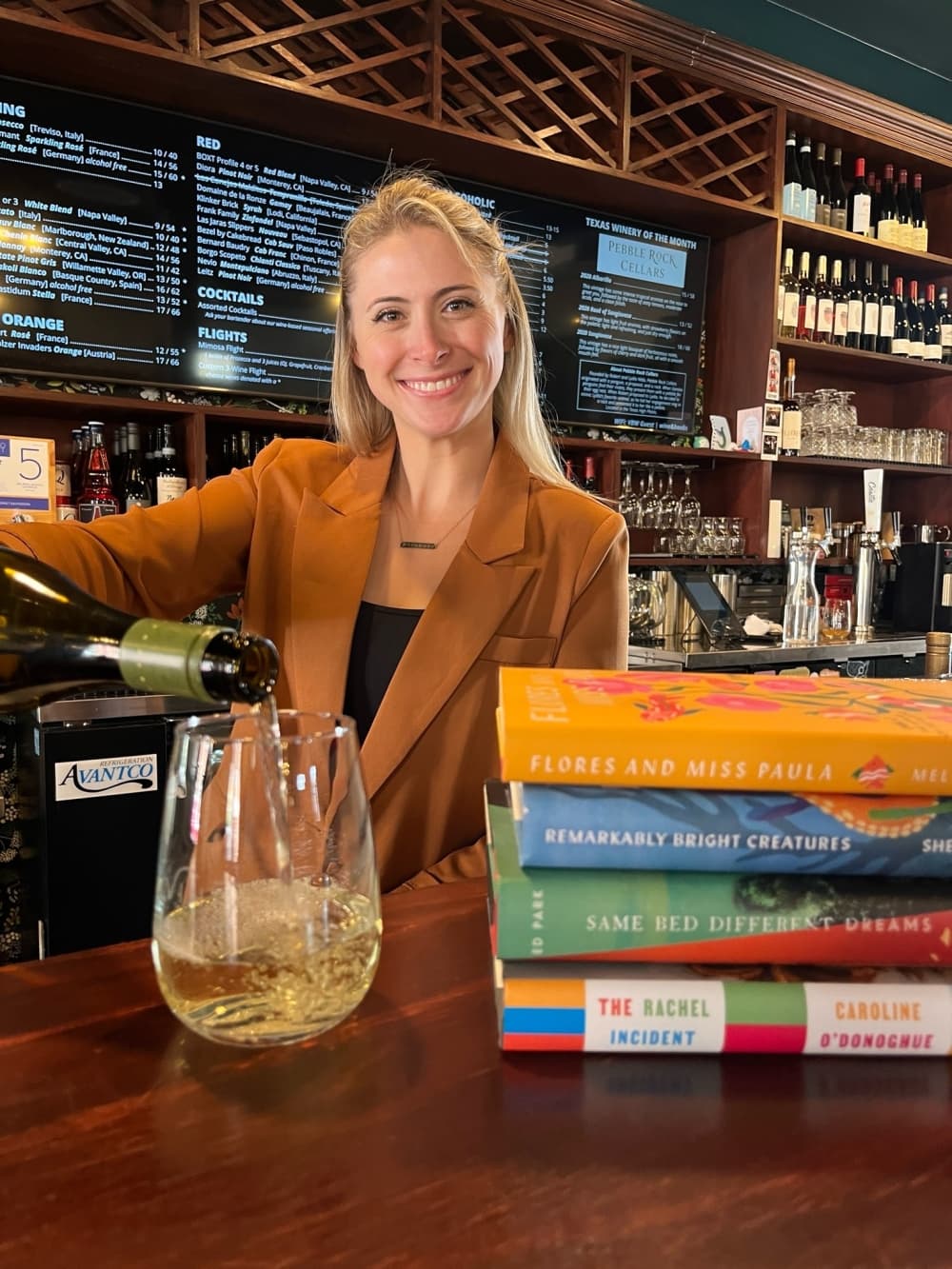 Owner Jean Buckner pours a glass of wine next to a stack of books.