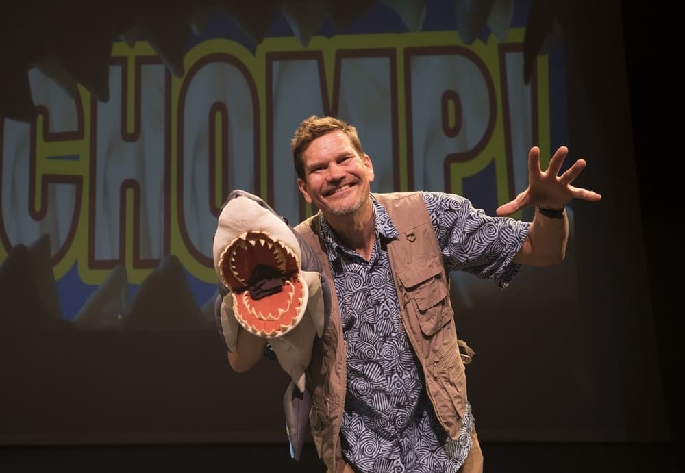 A man holding a hand puppet poses for a photo on stage.