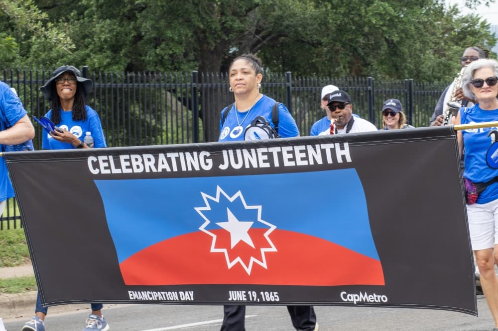 People walk in a parade holding a "Celebrating Juneteenth" banner.