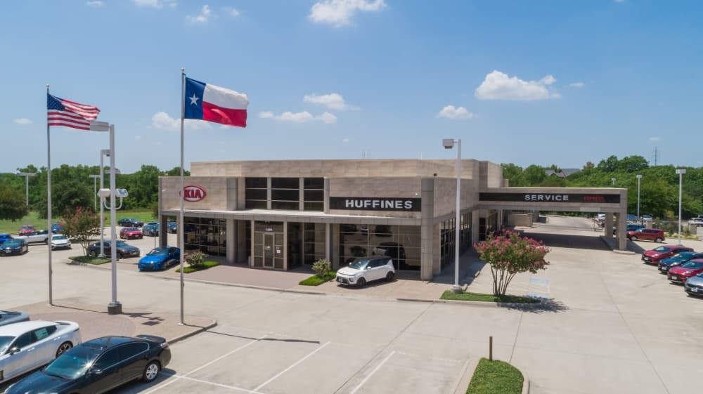 Exterior of a car dealership with American and Texas flags flying in front of building. 