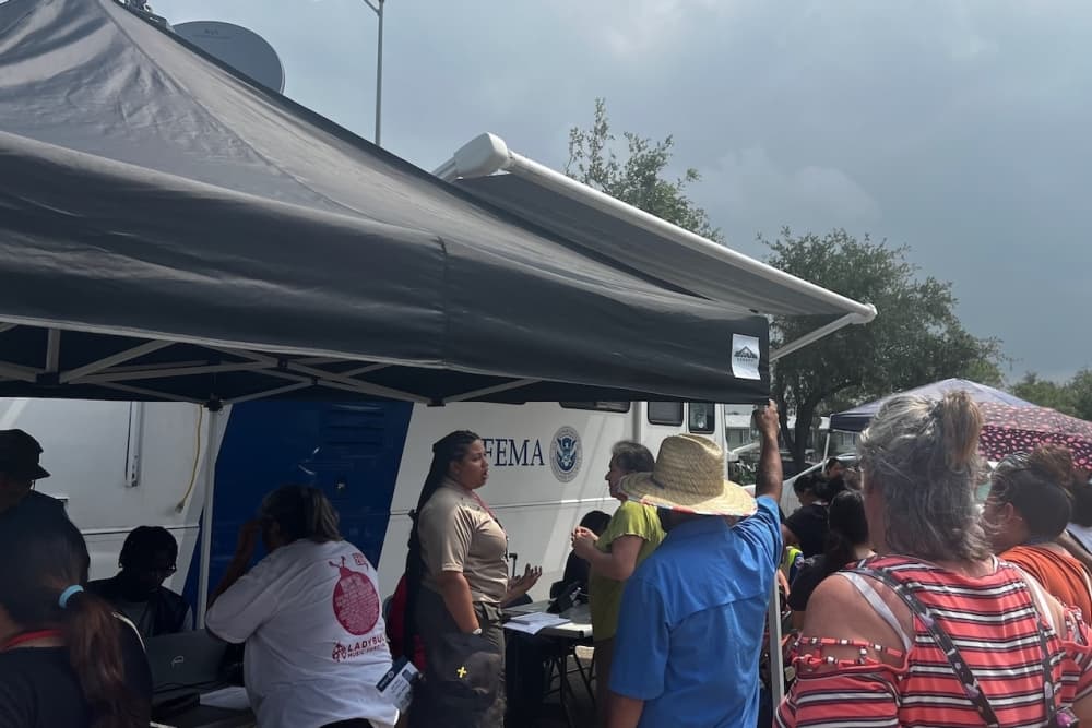 A line of people file outside the FEMA trucks.