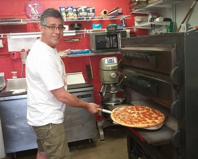 man putting pizza in overn