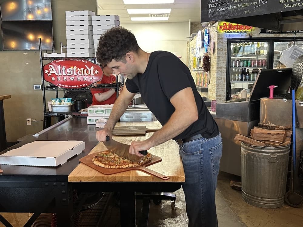 Image shows Angel Gomez slicing a pizza.