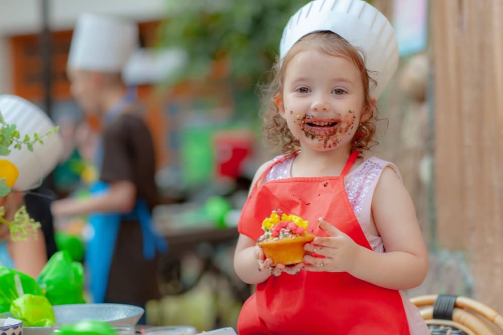Young girl wearing chef hat and holding a cupcake. 