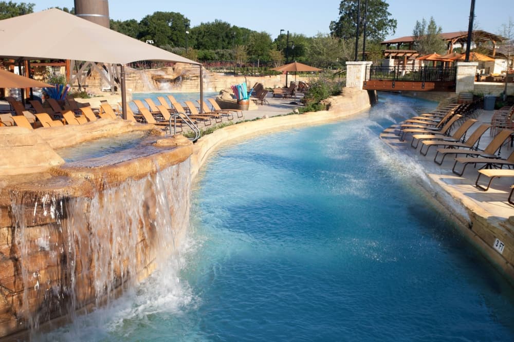 A lazy river with a rock water feature and pool chairs on either side