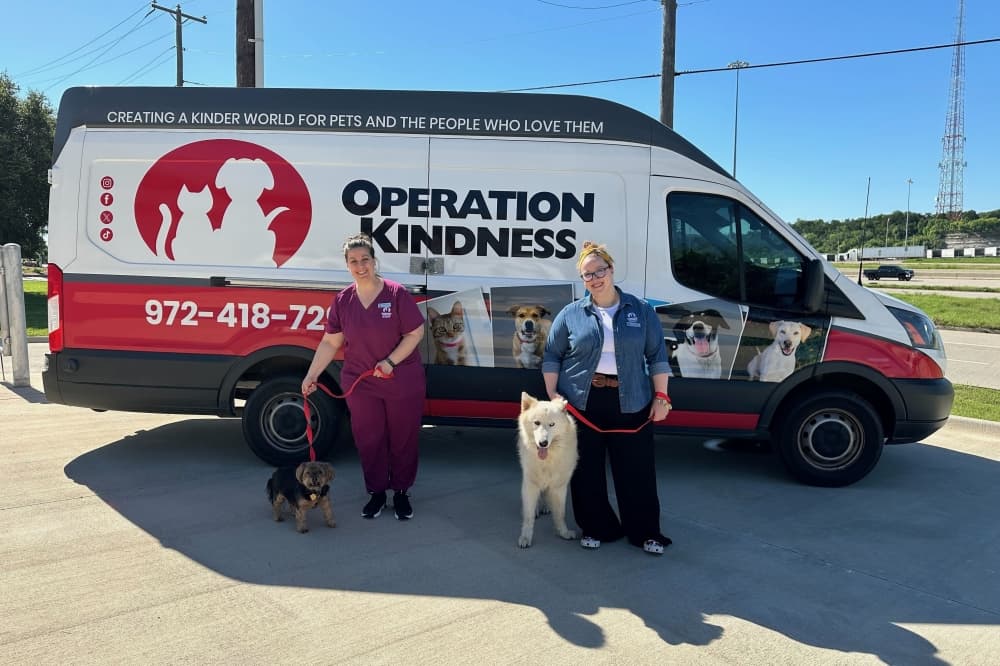 Two Veterinarians pose with dogs in front of an Operation Kindness van at the Lifesaving Partnerships Hub grand opening in Dallas. 